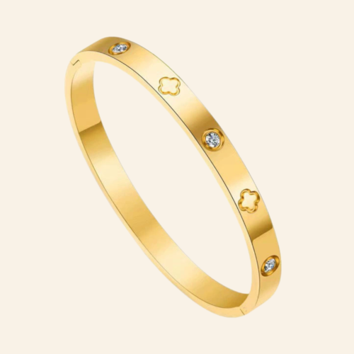 A model wearing the luxury gold clover bangle stacked on a wrist against a neutral silk background