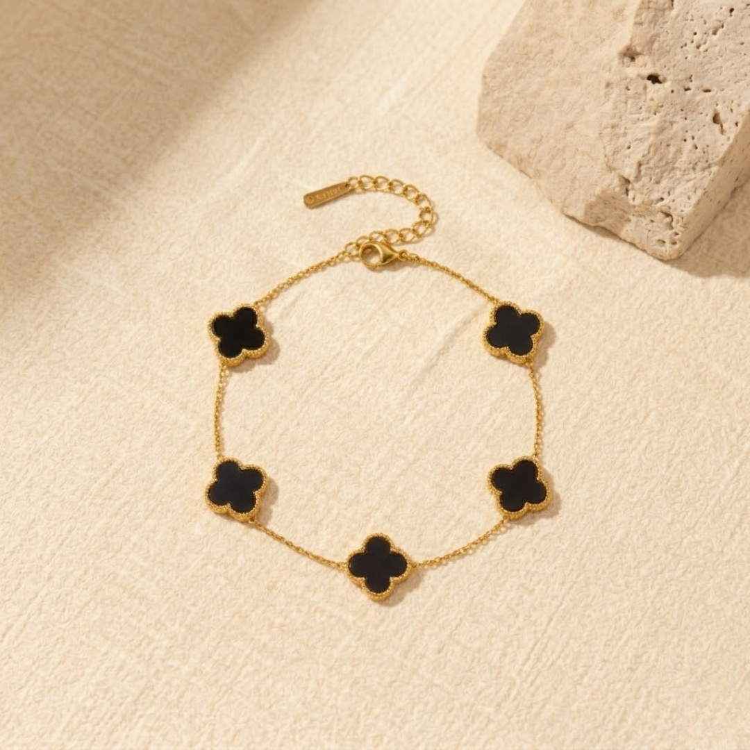 The Gift Maison 18K gold multi motif black clover bracelet on a neutral stone backdrop